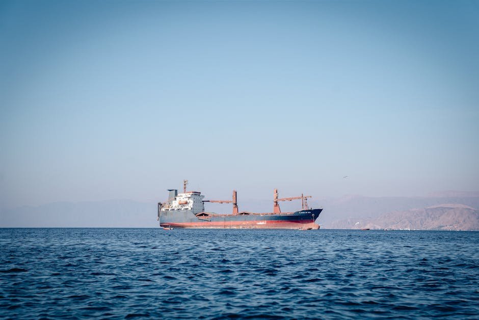 A cargo ship sailing on calm ocean waters under a clear blue sky.